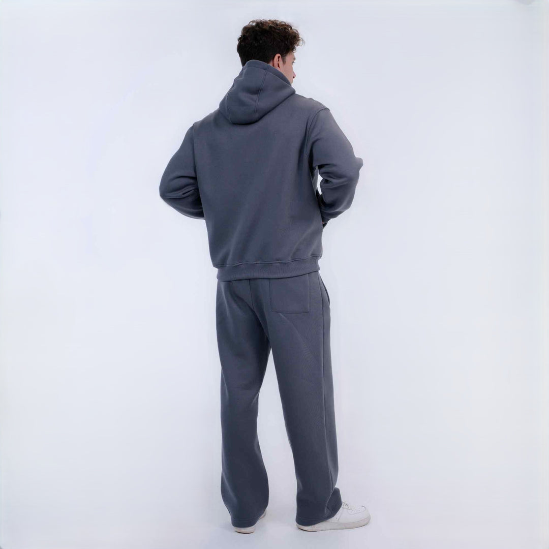 A man viewed from behind wearing a matching dark gray hoodie and sweatpants set, standing against a plain light gray studio background.
#color_gray