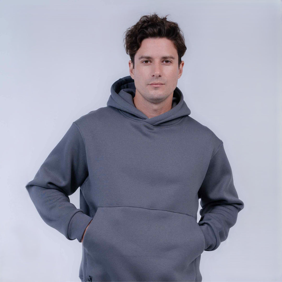 A man wearing a solid dark gray pullover hoodie with a front kangaroo pocket, standing against a light gray studio background.
#color_gray