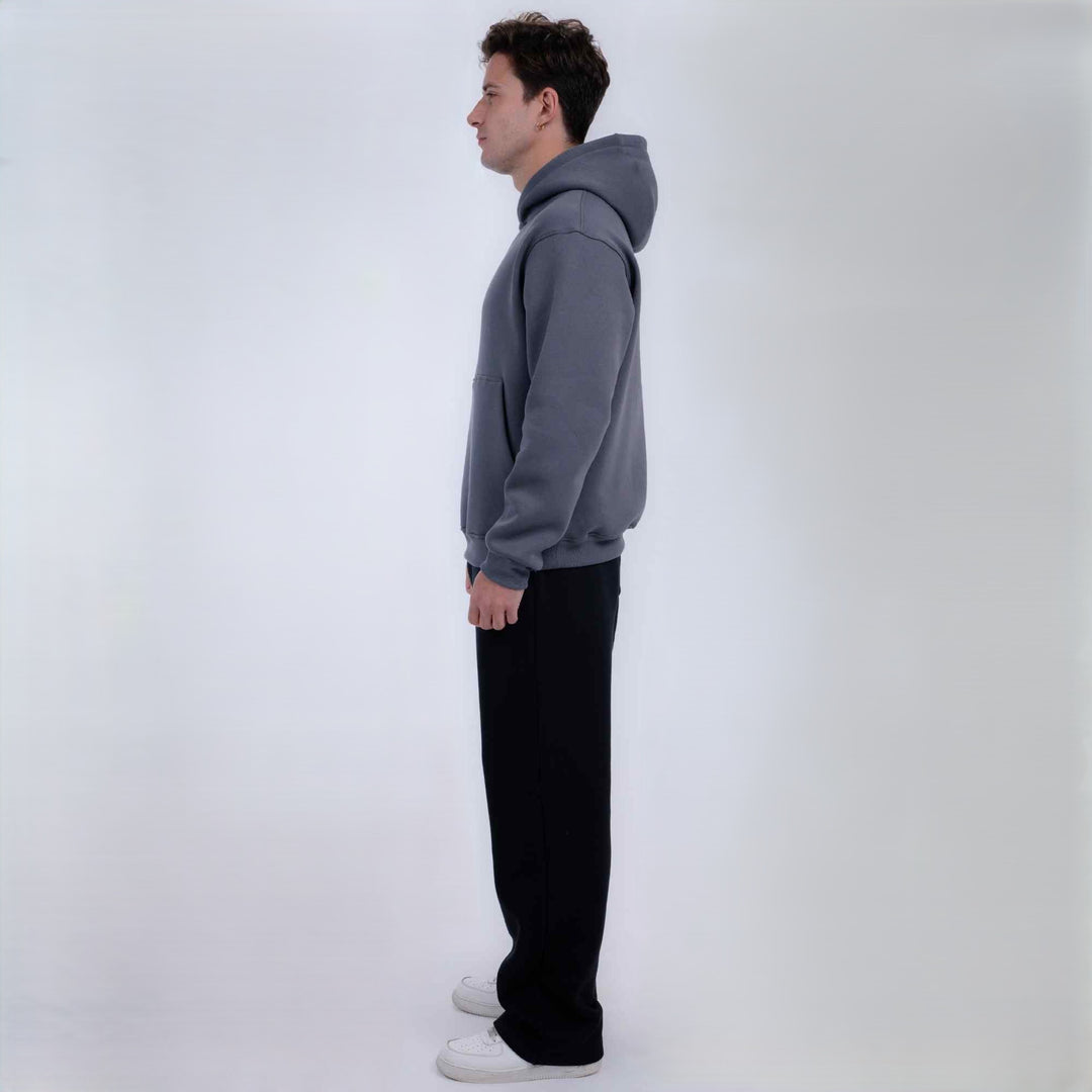A man in profile wearing a gray pullover hoodie, black pants, and white sneakers, standing against a plain light gray studio background.
#color_gray