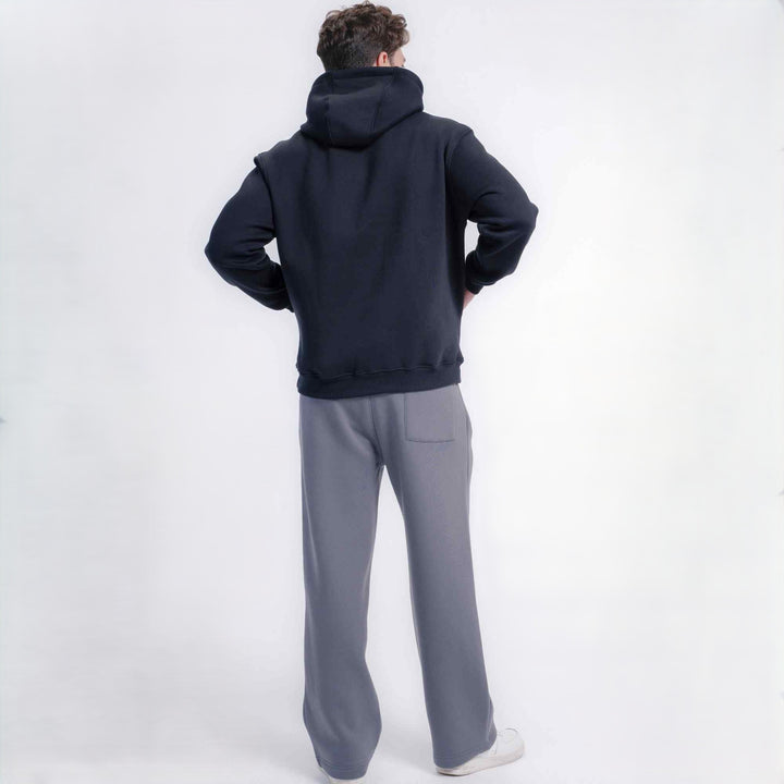 A man viewed from behind wearing a Black pullover hoodie and light gray wide-leg sweatpants, standing against a plain white studio background.
#color_black