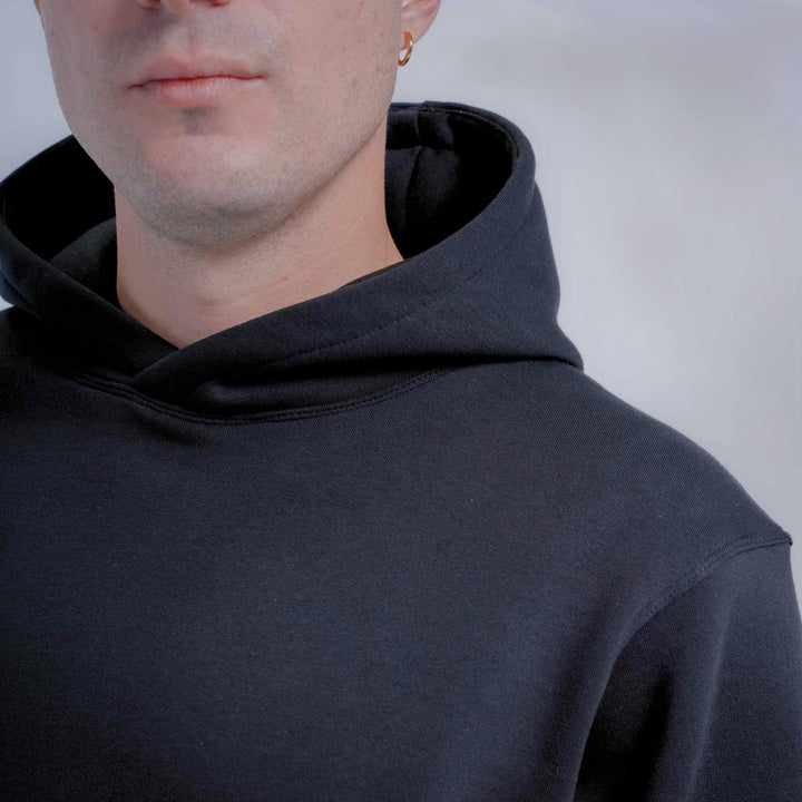 Close-up of a person wearing a black pullover hoodie against a light gray background.
#color_black