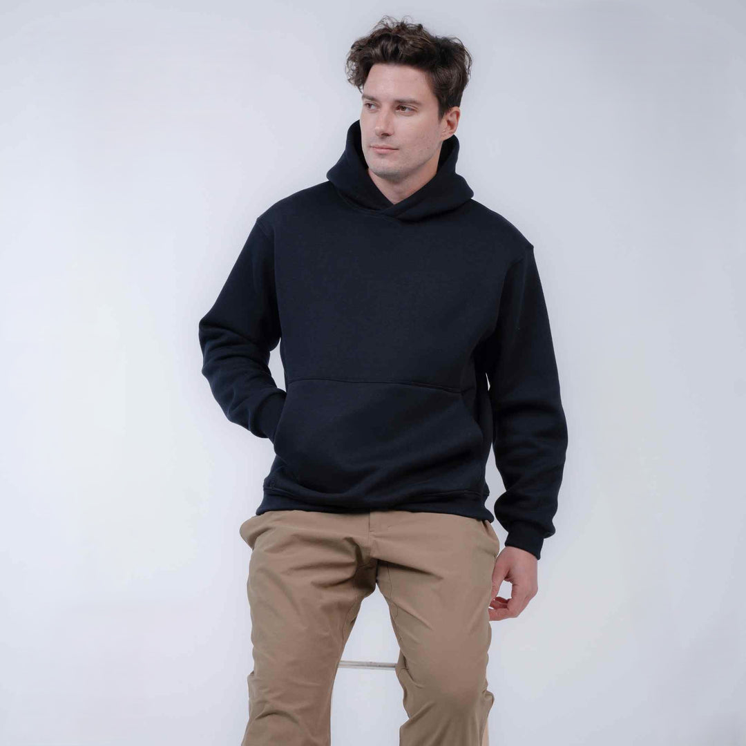 A man wearing a black pullover hoodie and tan pants, standing against a plain light gray studio background.
#color_black