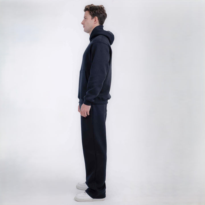 A man in profile wearing a dark navy blue hooded sweatshirt and matching sweatpants, standing against a clean white studio background.
#color_black