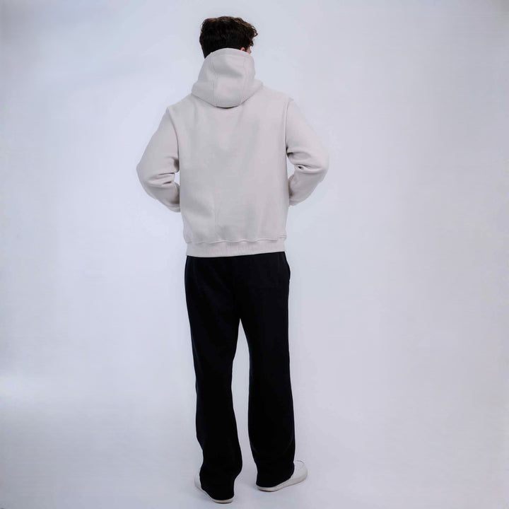 A person shown from the back wearing a light gray hooded sweatshirt and black pants, standing against a plain light gray studio background.
#color_cloud-dancer
