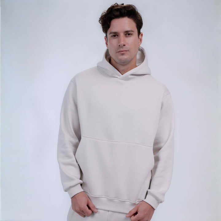 A man wearing a light beige pullover hoodie with a front kangaroo pocket, photographed against a clean, light gray studio background.
#color_cloud-dancer