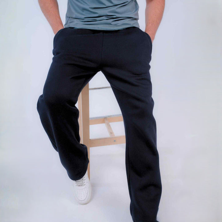 A person wearing black sweatpants and a gray t-shirt, sitting on a wooden stool against a white studio 
background.
#color_black