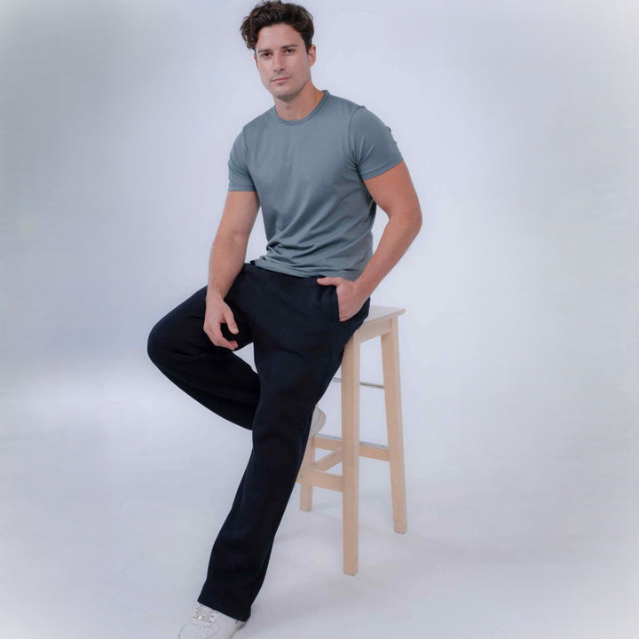A man wearing a slate sage green crewneck t-shirt and Black pants, sitting on a light wood stool against a light gray studio background.
#color_black