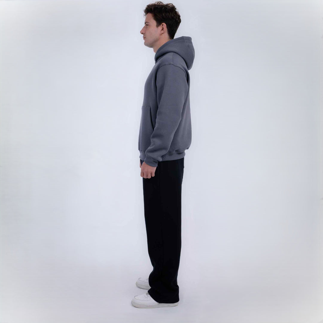 A man in profile wearing a gray pullover hoodie, black pants, and white sneakers, standing against a plain light gray studio background.
#color_black