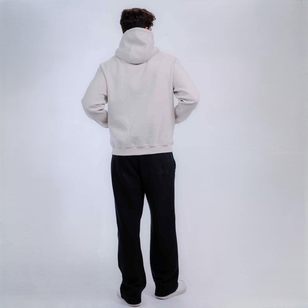 A person viewed from behind wearing a light off-white hooded sweatshirt and black pants, standing against a plain light gray studio background.
#color_black