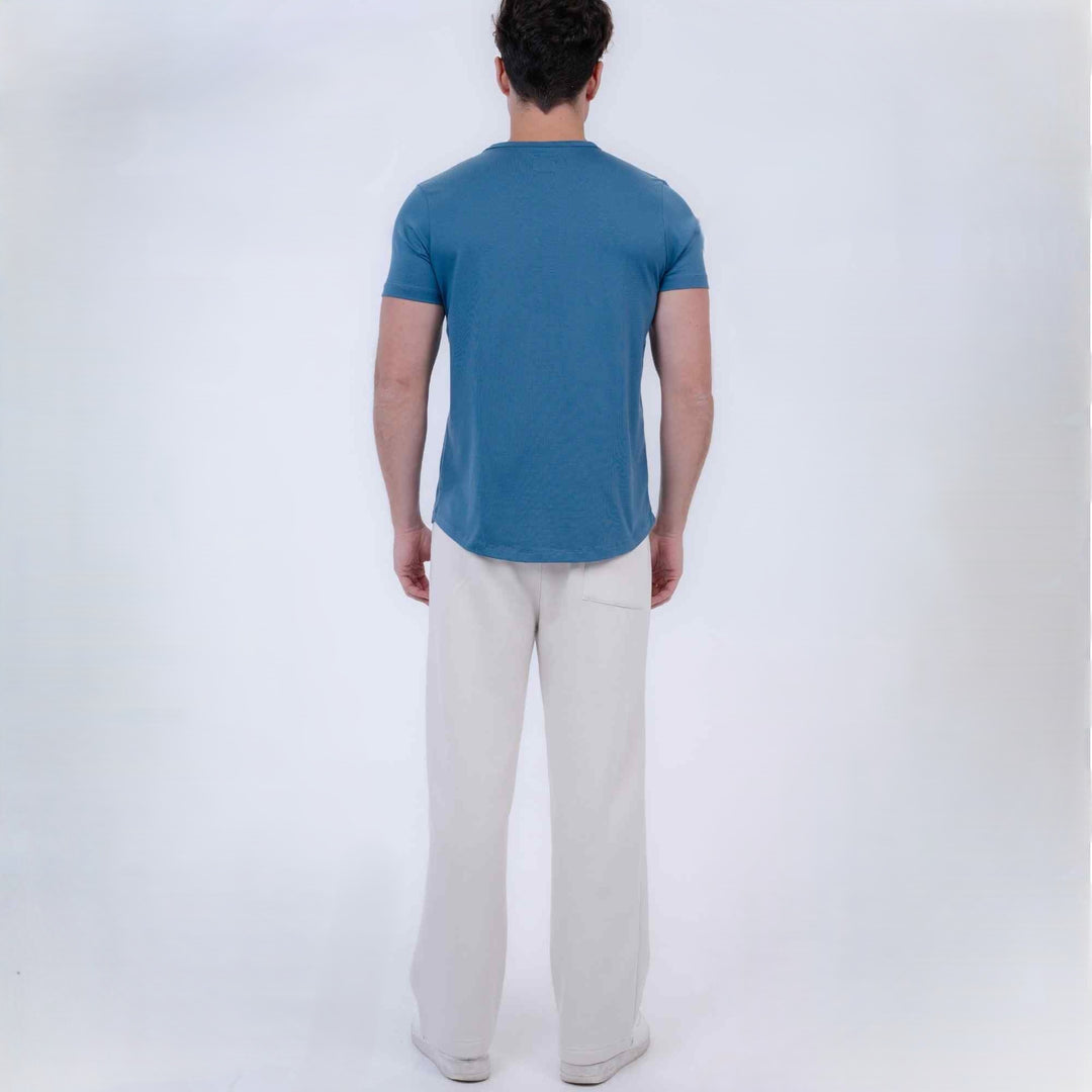 A man viewed from behind wearing a blue short-sleeve t-shirt and off-white trousers, standing against a plain light gray studio background.
#color_cloud-dancer